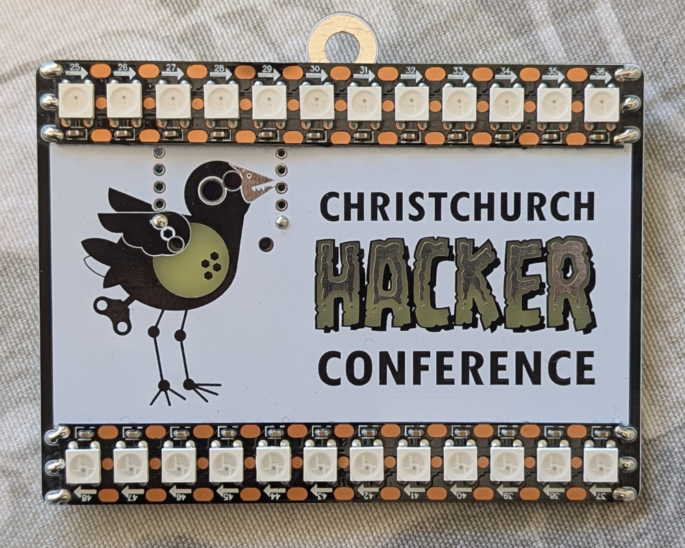 Front side of a circuit board conference attendee badge, showing a pukeko logo and mounted LED strips